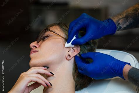 Portrait Of A Woman Getting Her Ear Pierced Man Showing A Process Of Piercing Ear Cleaning