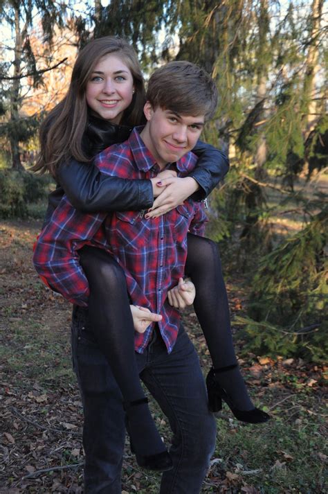 A Man And Woman Are Sitting On Top Of Each Other In The Woods With Trees Behind Them