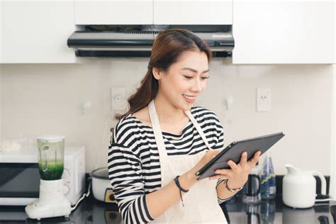 Young Asian Woman Using A Tablet Computer To Cook In Her Kitchen Stock