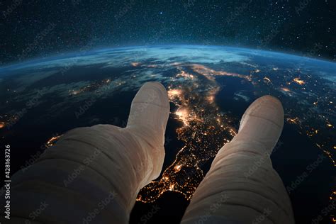 Spaceman Sits And Looks At The Blue Planet Earth With Night Lights Of Cities From Space