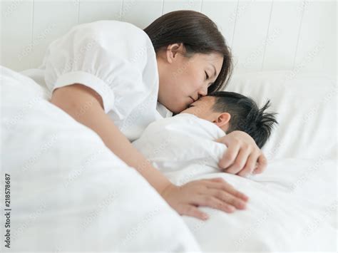 Beautiful Asian Mother Giving Good Night Kiss To Her Sleeping Son In