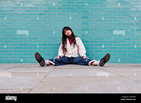 Beautiful Young Woman Sitting With Legs Apart In Front Of Brick Wall