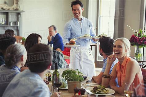 Smiling Waiter Serving Food To Friends Dining At Restaurant Table
