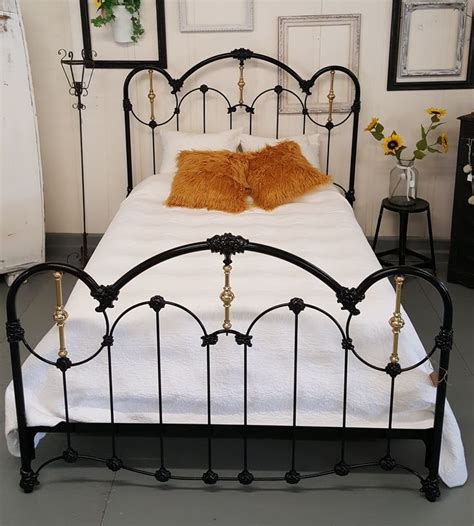 A Black Iron Bed With White Sheets And Orange Pillows On It S Headboard