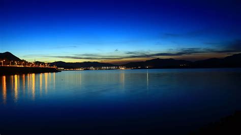 Lake Embankment Lights Mountains Under Blue Sky Reflection On Water 4k