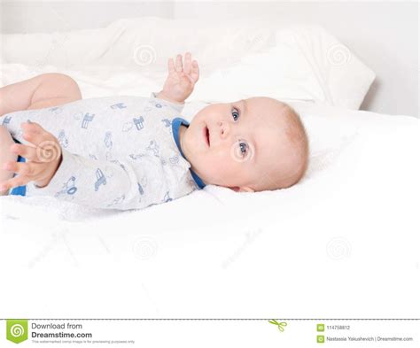 Portrait Of Sweet Newborn Infant Lying Quietly On White Bed Serious