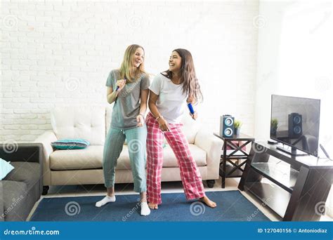 Cheerful Women Singing Karaoke And Dancing In Living Room Stock Photo