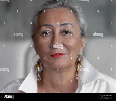 Portrait Of A Beautiful Mature Woman In A White Shirt With Long Earrings On A Light Background
