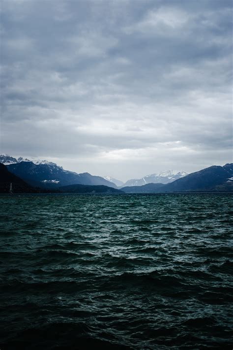 Body Of Water Near Mountain Under Cloudy Sky · Free Stock Photo