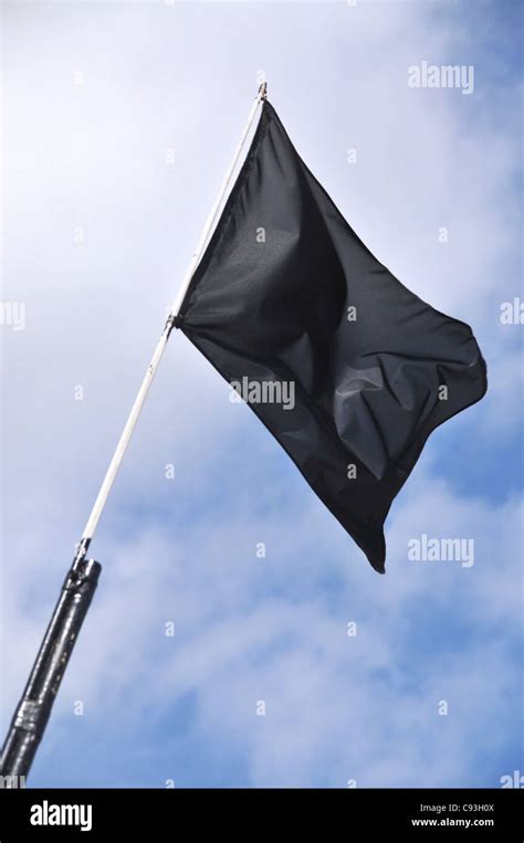 A Blank Black Flag Flying In The Wind Against A Cloudy Blue Sky Stock