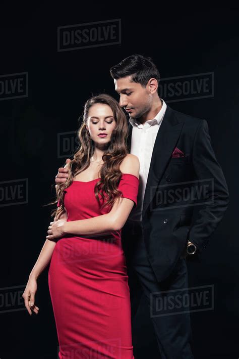 Handsome Man Embracing Beautiful Woman In Red Dress Isolated On Black