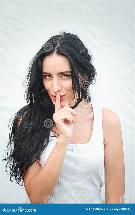 Girl Presses Index Finger To Her Lips Portrait Of A Beautiful Young Woman In A White T Shirt