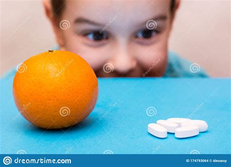 White Oval Pills And Ripe Orange Lie In The Face Of A Child On A Blue