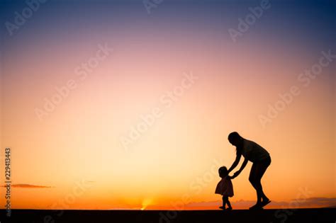 Silhouette Of Mother Teaching Her Child To Walk Stock Photo And