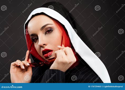 stylish demoniacal nun with red eyes posing in black suit red sunglasses and scarf stock image