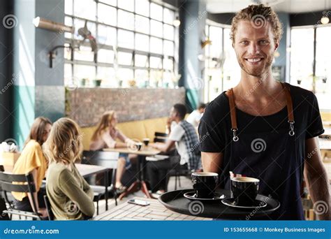 Portrait Of Waiter Serving Customers In Busy Coffee Shop Stock Photo