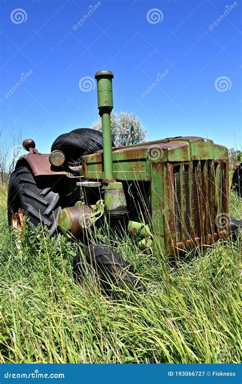 Old Forgotten Tractor Left In The Long Grass Of A Salvage And Junkyard