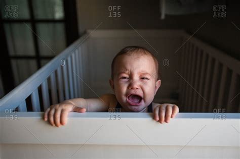 Baby Crying While Holding Onto Edge Of Crib Stock Photo