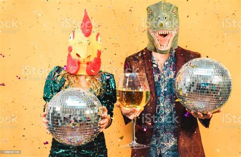 Crazy Young Couple Having Fun For New Years Eve Party Wearing Trex And Chicken Mask Fashion