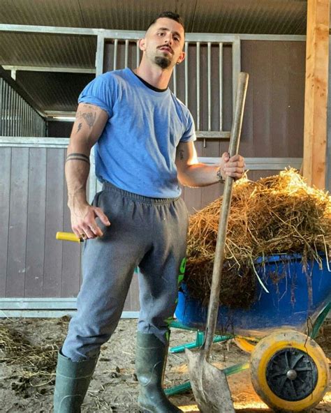 a man standing next to a wheelbarrow full of hay and holding a shovel