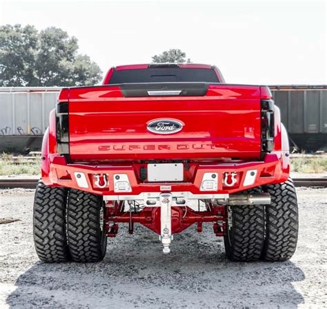 The Rear End Of A Red Pickup Truck Parked On Top Of A Gravel Road Next