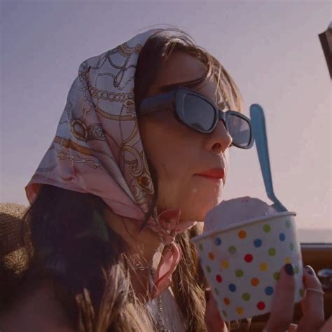 A Woman Wearing Sunglasses And A Scarf Drinking From A Paper Cup While