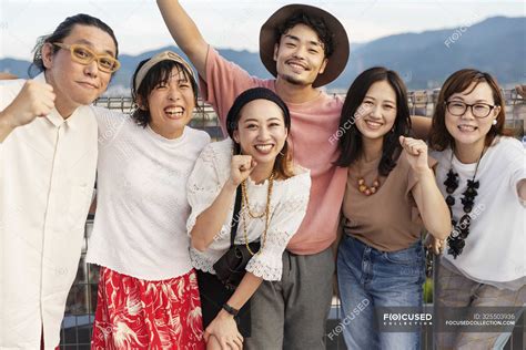 Smiling Group Of Young Japanese Men And Women Standing On Rooftop In