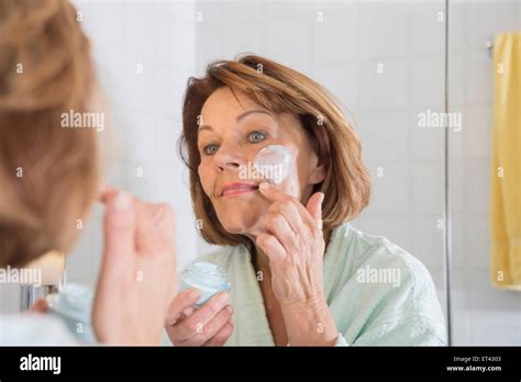 Reflection Of A Senior Woman Applying Moisturizer On Her Face In Mirror