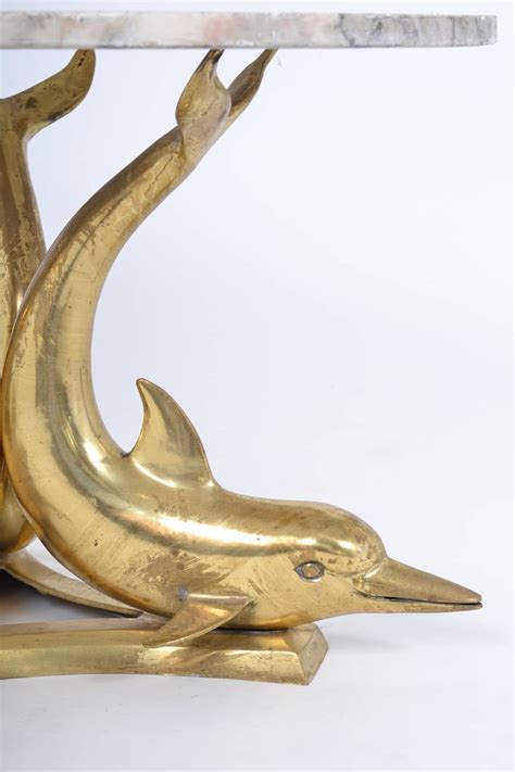 This coastal coffee table has a curved oval glass table top and a carved sculpture base with 2 swimming dolphin figures. Marble Top Gilt Bronze Dolphin Coffee Table at 1stDibs