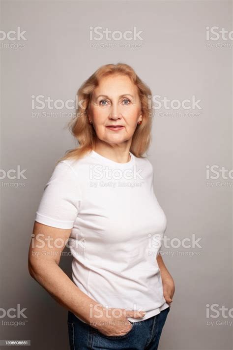 Happy Mature Old Adult Woman Wearing White Tshirt Standing Against Gray