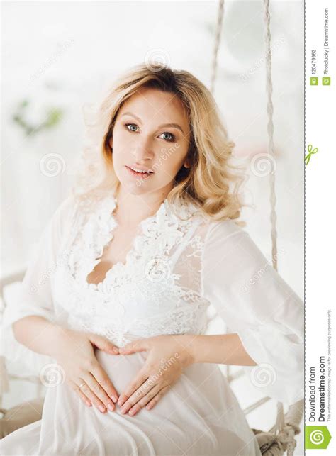 Beautiful Blonde Pregnant Woman Sitting At Swing With Flowers Stock