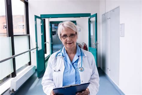 Confident Female Doctor With Clipboard Standing In Hospital Corridor