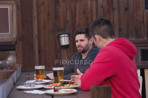 Friends Talking With Each Other While Having Drinks At Outdoor Pub