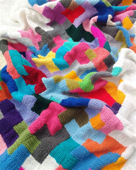 A Multicolored Knitted Blanket Laying On Top Of A Bed