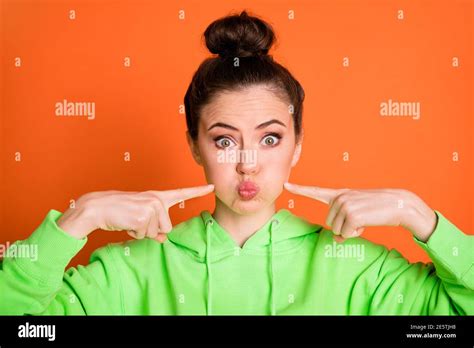 Photo Portrait Of Pouting Girl Pushing Fingers Into Puffed Cheeks Isolated On Vivid Orange