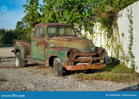 Rusted Vintage Chevrolet Pickup Truck Parked By A White Fence