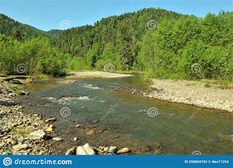 The Bend Of A Shallow Stormy River With Rocky Banks Flowing Down From