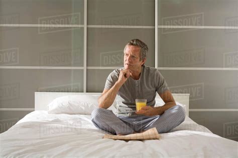 Puzzled Senior Man Sitting Cross Legged On Bed With Hand On Chin
