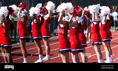 High School Cheerleaders Holding Their Pompoms In The Air While Cheering During A Football Game
