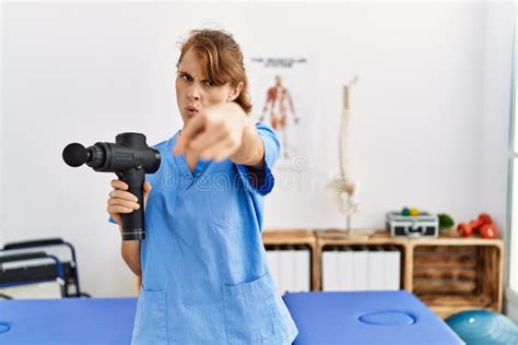 Beautiful Caucasian Woman Holding Therapy Massage Gun At Wellness Center Pointing With Finger To