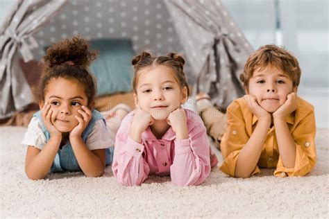 Adorable Multiethnic Children Lying On Carpet And Looking Stock Image