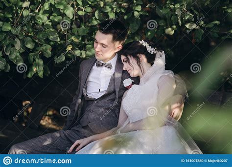 Newlyweds Sitting On A Bench They Look At Each Other In Love Stock