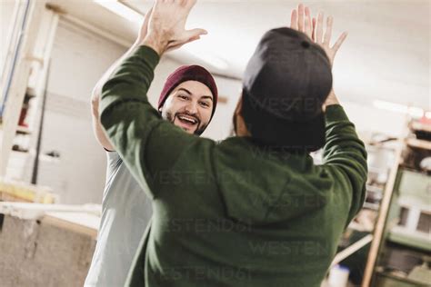 Two Happy Young Men High Fiving In Workshop Stock Photo