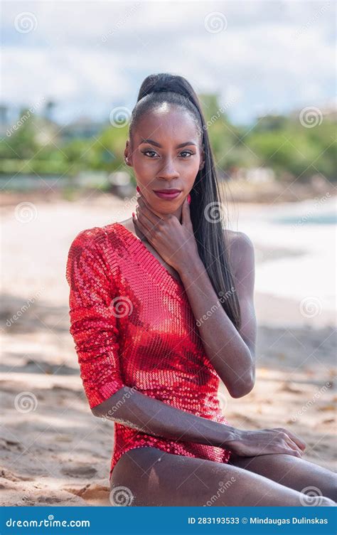 portrait of beautiful caribbean adult teen in barbados wearing red bikini and sitting on a
