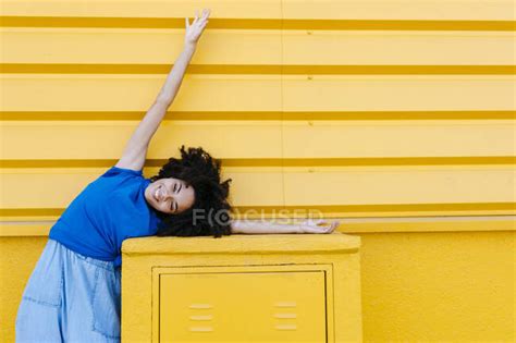 Dreamy Woman Bending Sideways Over Platfrom In Front Of Yellow Wall Emotion Curly Hair