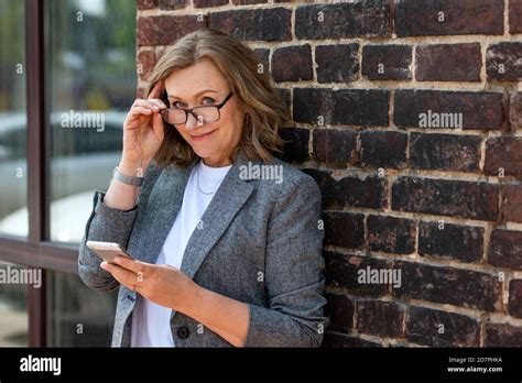 Portrait Of A Happy Beautiful Blonde Woman 55 Years Old Smiling With A Smartphone In Hand