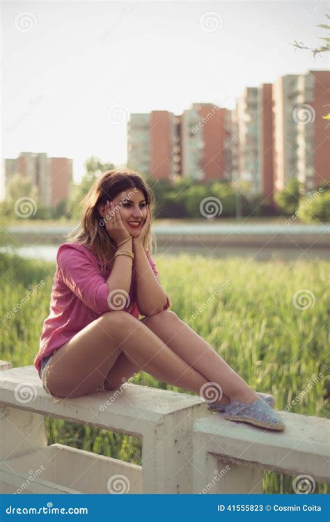 Beautiful And Attractive Woman Sitting On A River Concrete Side Wearing Casual Denim Shorts
