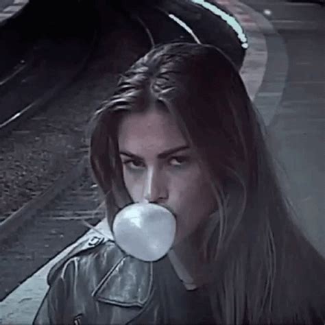 A Woman With Long Hair Blowing A Bubble In Front Of Her Face On A Train