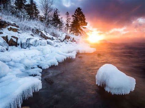 The Sun Is Setting Over An Icy Lake With Ice On It And Trees In The