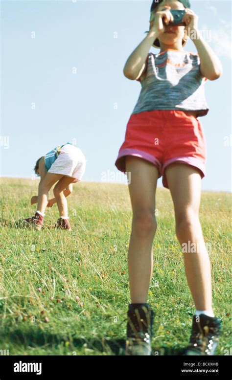 Girl Taking Photo Second Child Bending Over Looking At Grass In